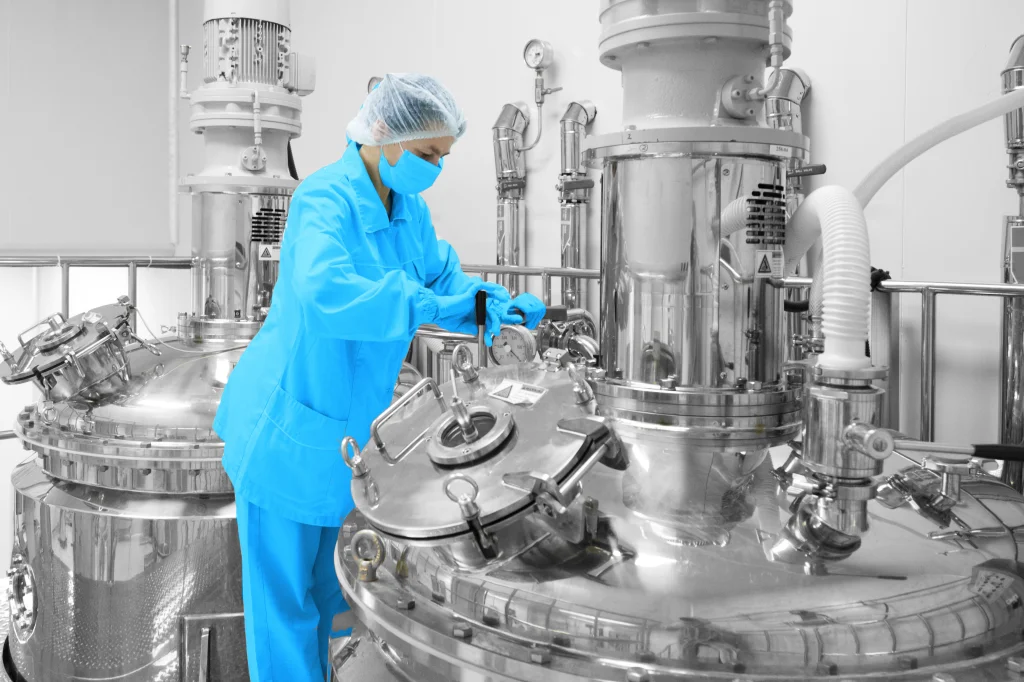 Technikerin in Schutzkleidung justiert sorgf&auml;ltig die Ausr&uuml;stung an einer hochmodernen automatisierten Produktionsanlage, symbolisch f&uuml;r die Optimierung und Weiterentwicklung von Fertigungsprozessen durch spezialisierte Automation und Industrial IT-L&ouml;sungen.